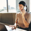 Lächelnde Frau mit dem Smartphone in der Hand. Sie nutzt onOffice enterprise am Laptop.