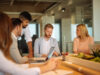 Five colleagues gathered around an office table for a meeting.